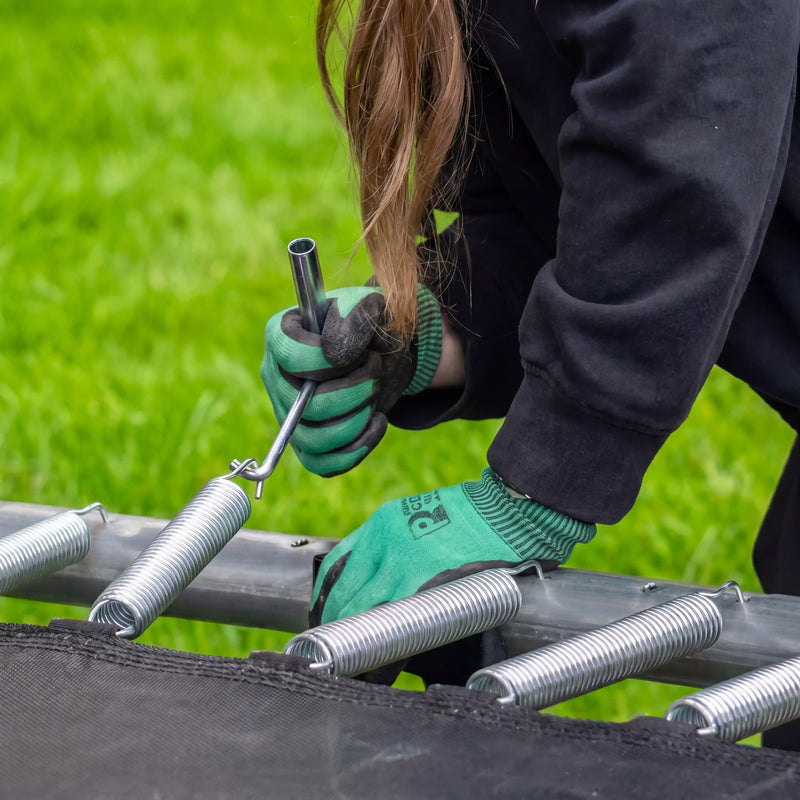Person wearing gloves using a tool on North trampoline springs against a green grass background
