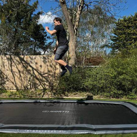 adult-jumping-on-north-17ft-x-12ft-rectangular-inground-trampoline-in-garden