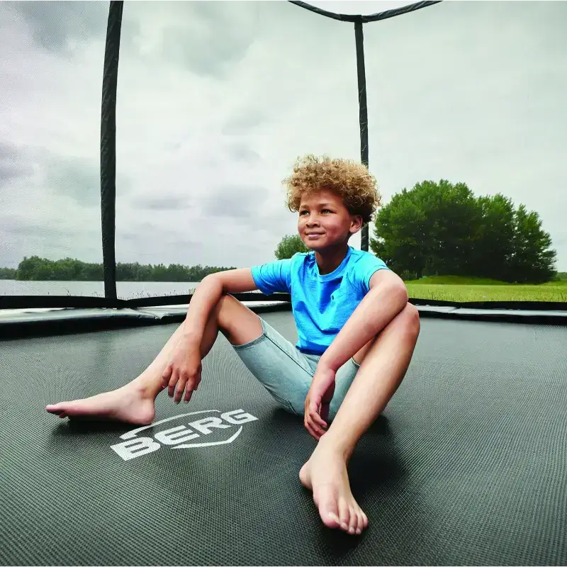 berg-ultim-elite-rectangular-trampoline-with-spacious-jumping-area-boy-sitting-on-berg-trampoline-with-safety-net