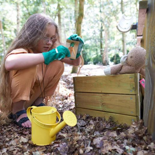 child-gardening-beside-wooden-planter-box-with-yellow-watering-can-and-toy-rabbit