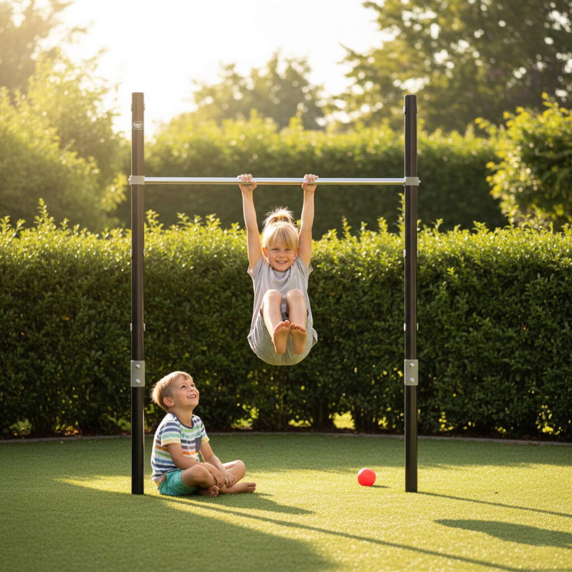 child-hanging-from-exit-ivy-tumble-bar-while-another-child-sits-below-in-garden