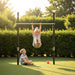 child-hanging-from-exit-ivy-tumble-bar-while-another-child-sits-below-in-garden