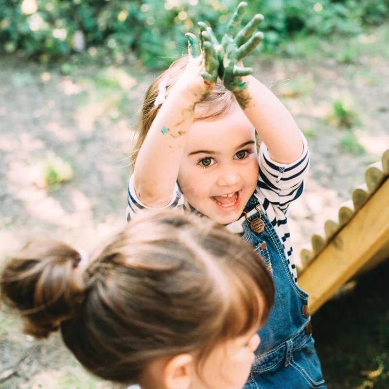 child-showing-muddy-green-hands-during-outdoor-play