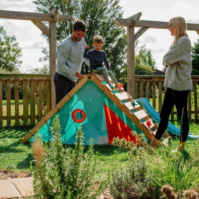 child-sitting-at-top-of-triangular-playcentre-ramp-with-two-adults-standing-nearby