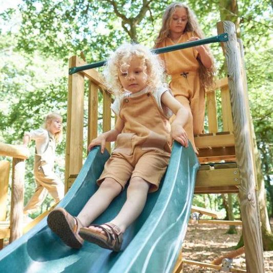 child-sliding-down-green-wave-slide-on-wooden-playcentre-with-other-children-waiting-above