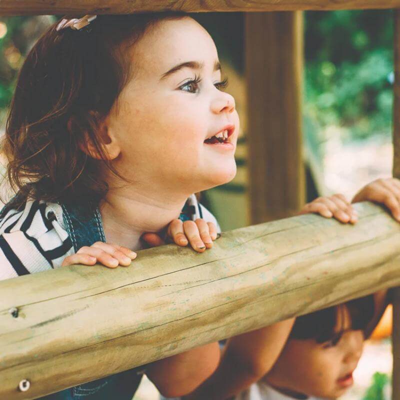 close-up-of-child-smiling-over-wooden-playcentre-railing