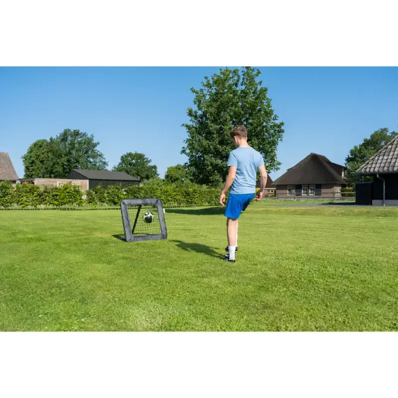 Lifestyle shot of EXIT Kickback adjustable sports rebounder with kid playing football.