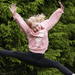 girl-jumping-outdoors-in-pink-hoodie-against-green-trees