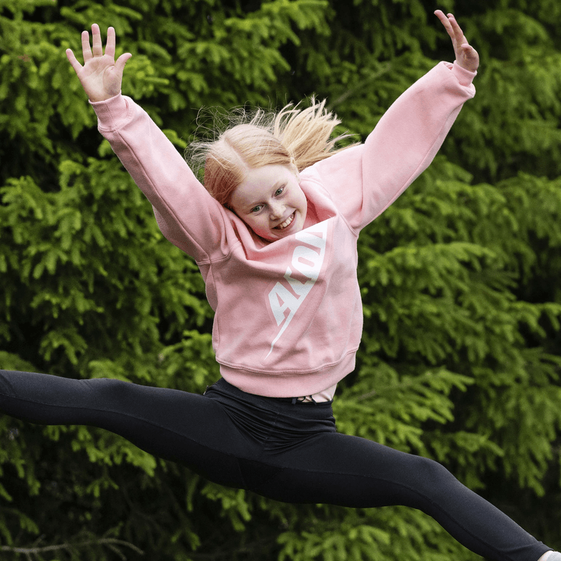 girl-jumping-outdoors-in-pink-hoodie-against-green-trees