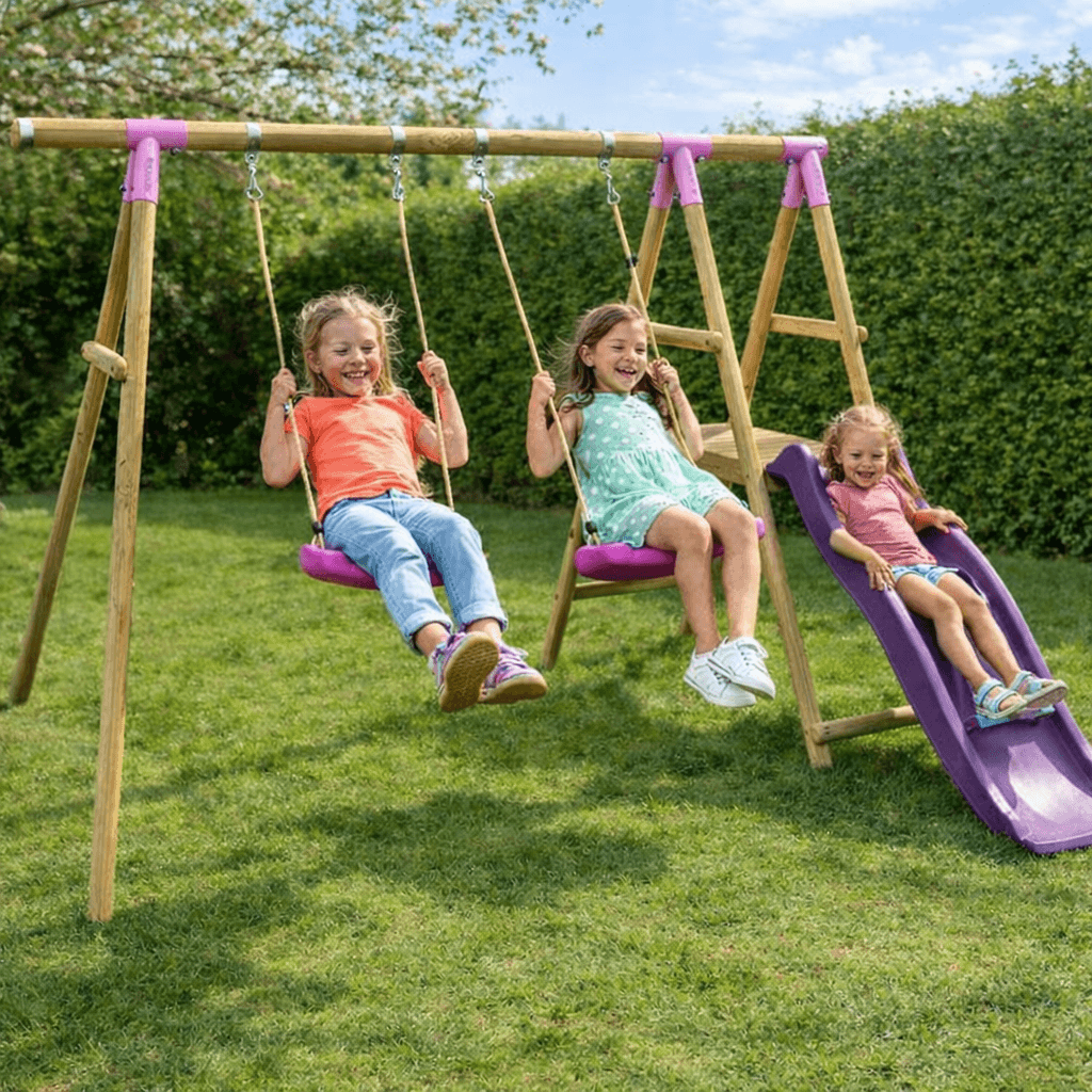 pink-wooden-swing-set-with-two-children-on-swings-and-one-child-on-purple-slide-in-garden