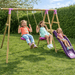 pink-wooden-swing-set-with-two-children-on-swings-and-one-child-on-purple-slide-in-garden