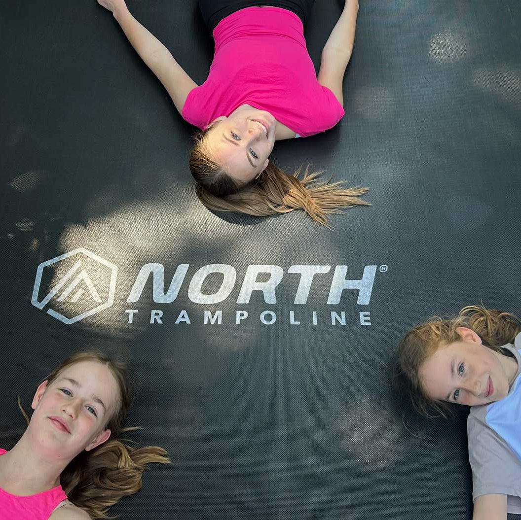 three-girls-lying-on-north-trampoline-jump-mat-with-logo-visible