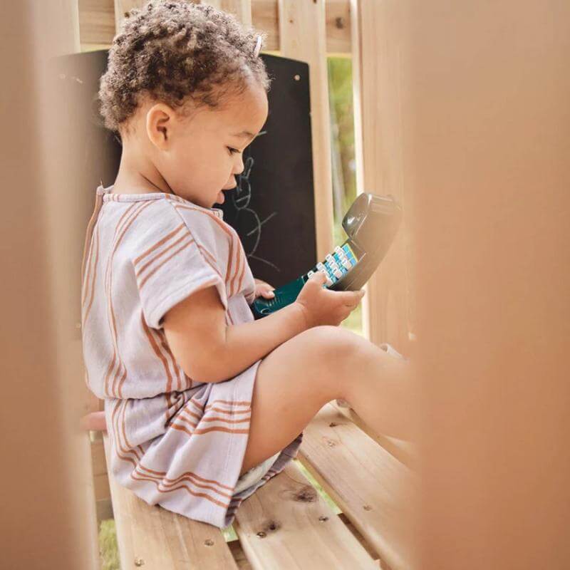 toddler-sitting-inside-wooden-playcentre-holding-toy-telephone-handset