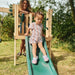 toddler-sliding-down-green-slide-on-wooden-playcentre-with-adult-behind