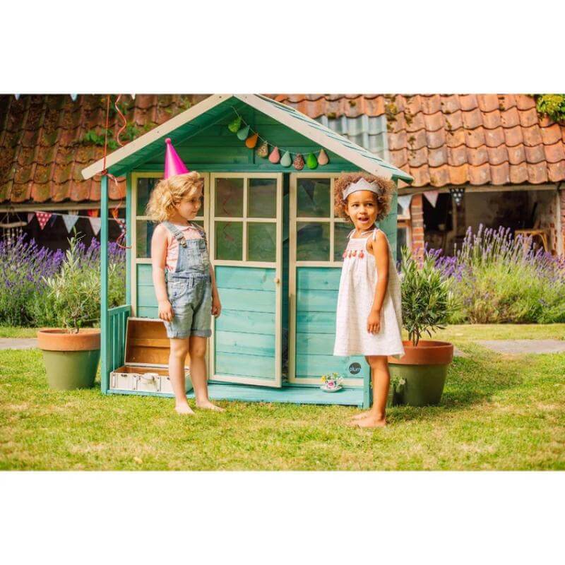 two-children-standing-outside-teal-wooden-playhouse-with-open-door