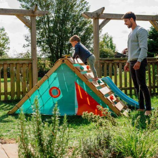 wide-view-of-child-climbing-triangular-playcentre-ramp-with-adult-standing-beside